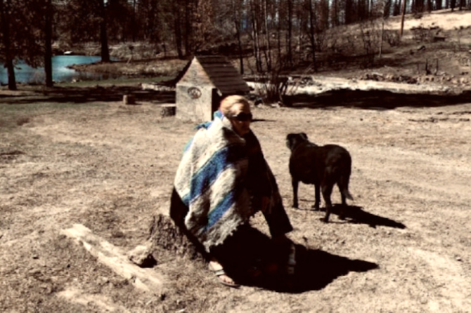 Terri Runft, of Chiloquin, sits on a stump in the empty lot that used to be her home before it was destroyed by the 242 Fire in 2020.