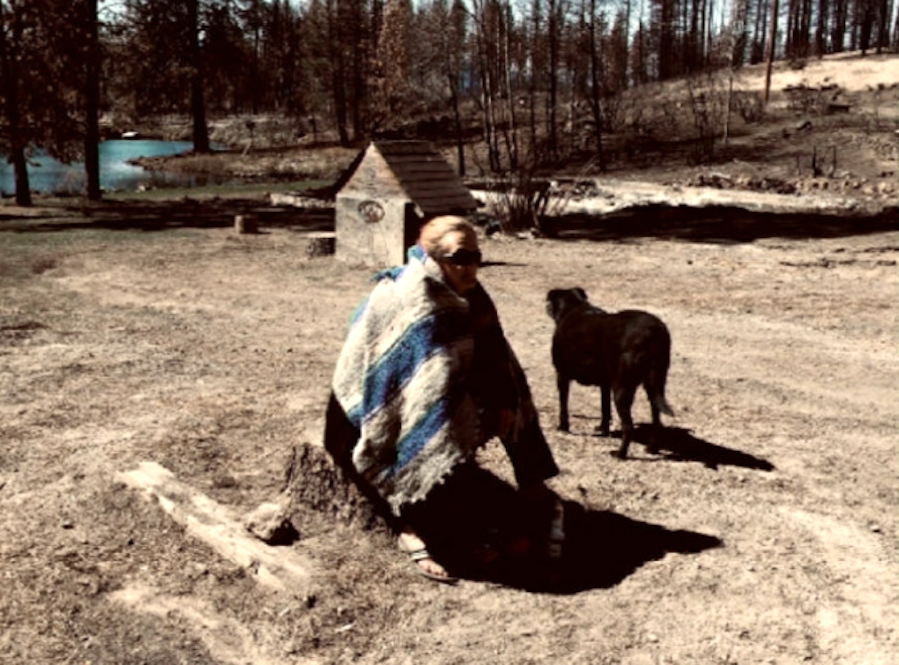 Terri Runft, of Chiloquin, sits on a stump in the empty lot that used to be her home before it was destroyed by the 242 Fire in 2020.